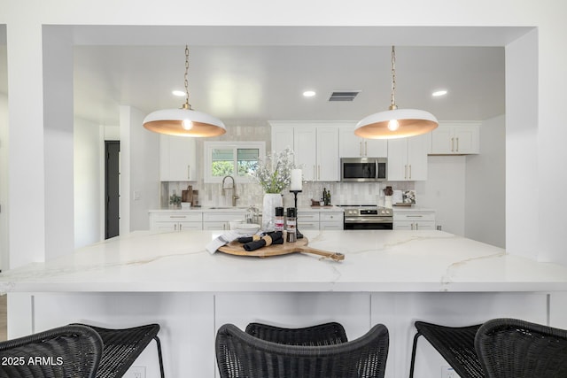 215 W Ruth Ave, Phoenix, AZ 85021 - kitchen featuring stainless steel appliances, white cabinetry, backsplash, decorative light fixtures, and a kitchen bar