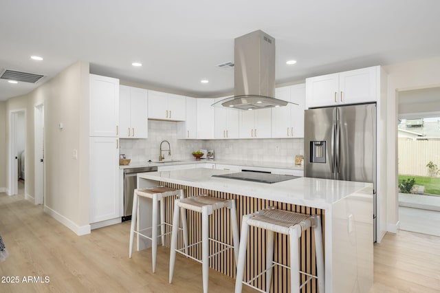 kitchen with a sink, appliances with stainless steel finishes, a kitchen bar, visible vents, and island range hood