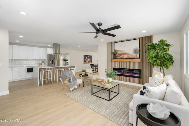 living area with recessed lighting, light wood-type flooring, visible vents, a ceiling fan, and a glass covered fireplace