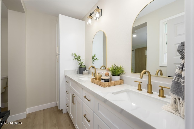 full bathroom featuring baseboards, double vanity, a sink, and wood finished floors
