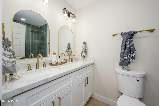 bathroom with double vanity, a sink, toilet, and tiled shower