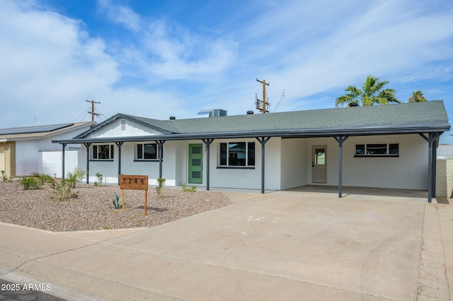 ranch-style house with a shingled roof, driveway, a carport, and stucco siding