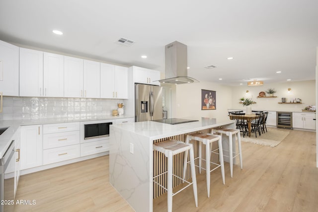 kitchen featuring tasteful backsplash, appliances with stainless steel finishes, white cabinetry, island range hood, and beverage cooler