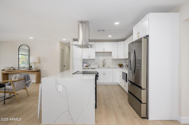 kitchen with light wood finished floors, stainless steel fridge, island exhaust hood, visible vents, and decorative backsplash