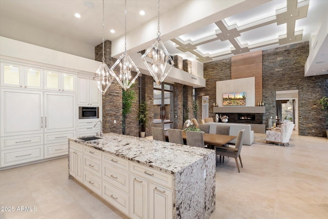 kitchen with a high ceiling, a sink, open floor plan, light stone countertops, and a center island with sink