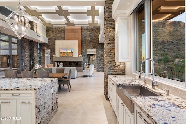 kitchen featuring a warm lit fireplace, open floor plan, decorative light fixtures, light stone countertops, and a sink