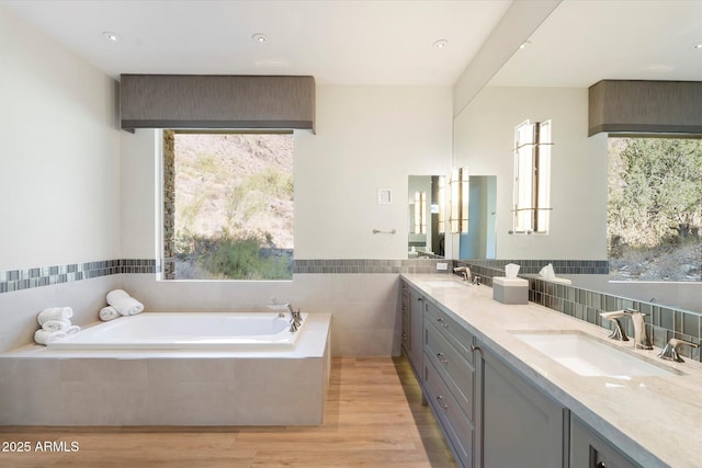 bathroom with double vanity, wood finished floors, a sink, and a bath