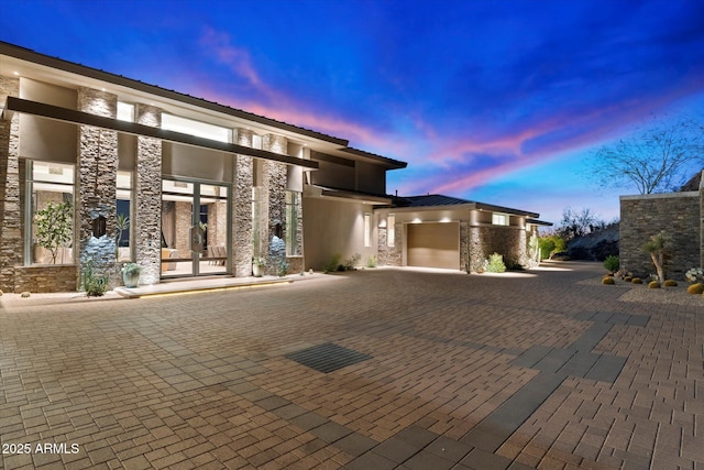 exterior space featuring a garage, stone siding, and decorative driveway