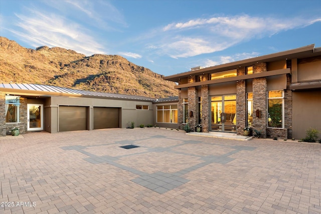 view of front facade with stucco siding, a standing seam roof, a mountain view, a garage, and stone siding