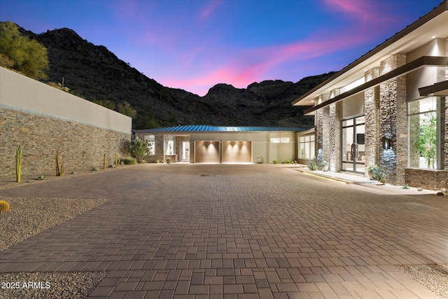 view of front of home featuring a garage, stone siding, a mountain view, and decorative driveway