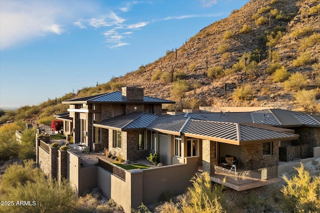 rear view of property with metal roof, stone siding, a standing seam roof, and fence private yard