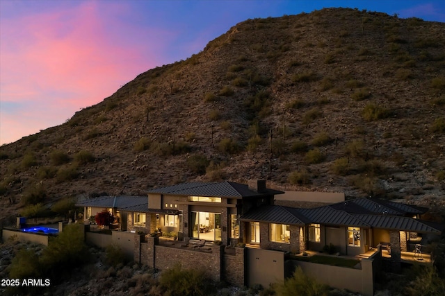 back of house at dusk featuring a patio, a chimney, a standing seam roof, a mountain view, and metal roof