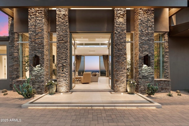 exterior entry at dusk featuring stone siding and a patio