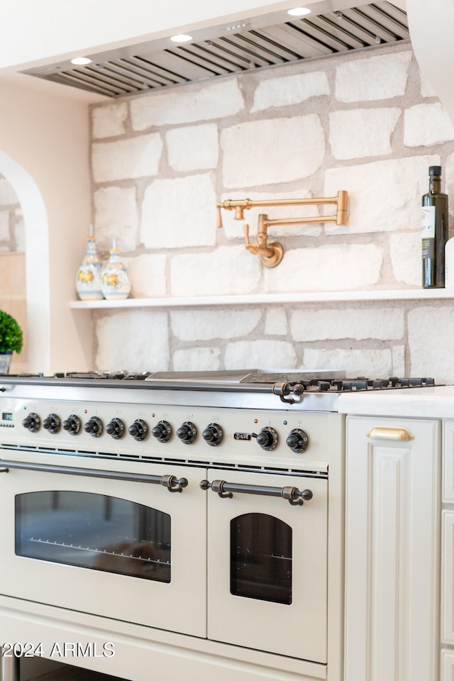 kitchen featuring high end white range, white cabinetry, and exhaust hood