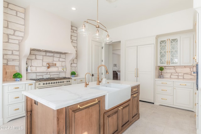 kitchen featuring light stone countertops, tasteful backsplash, sink, a center island with sink, and white cabinetry