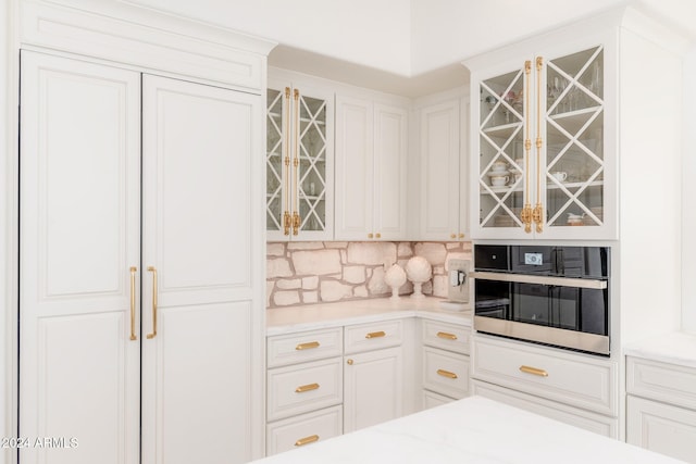 kitchen with white cabinets, decorative backsplash, and stainless steel oven