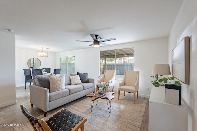 living room featuring light wood finished floors, baseboards, and ceiling fan with notable chandelier