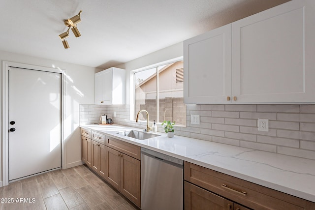 kitchen with a sink, stainless steel dishwasher, decorative backsplash, light stone countertops, and light wood finished floors