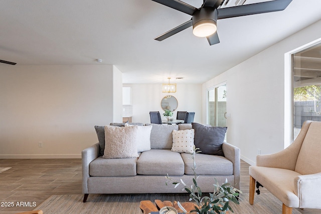 living room featuring plenty of natural light, baseboards, wood finished floors, and ceiling fan with notable chandelier