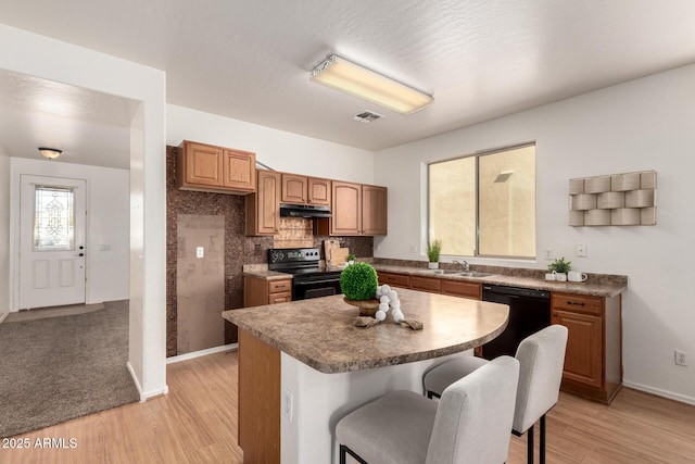 kitchen with under cabinet range hood, a breakfast bar, a kitchen island, black appliances, and brown cabinetry