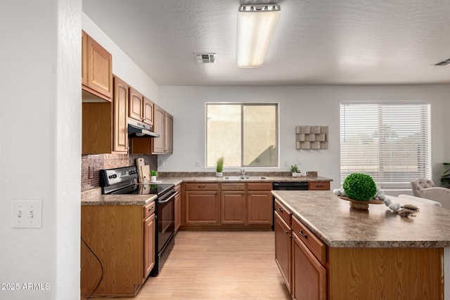 kitchen featuring black electric range, visible vents, a sink, light wood-type flooring, and under cabinet range hood