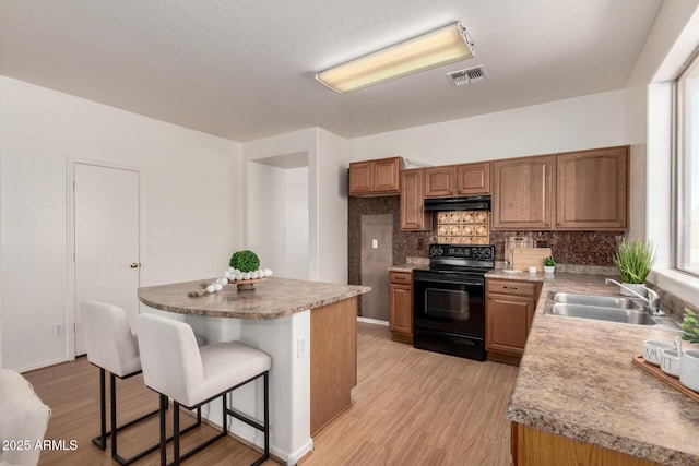 kitchen featuring visible vents, brown cabinets, black electric range oven, under cabinet range hood, and a sink