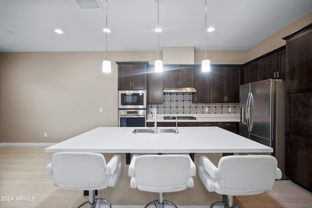 kitchen featuring decorative backsplash, dark brown cabinetry, pendant lighting, and an island with sink