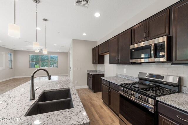 8313 E Impala Ave, Mesa, AZ 85209 - kitchen with stainless steel appliances, a sink, dark brown cabinets, light wood finished floors, and decorative backsplash