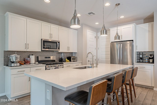 kitchen featuring appliances with stainless steel finishes, pendant lighting, white cabinets, and an island with sink