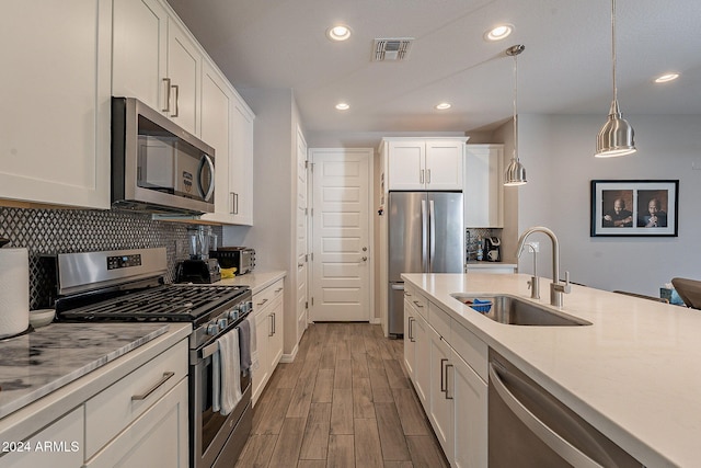 kitchen featuring hanging light fixtures, sink, light wood-type flooring, white cabinetry, and appliances with stainless steel finishes