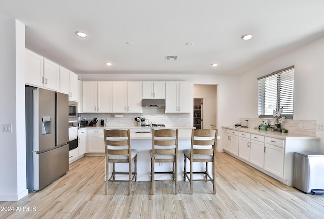 kitchen featuring a breakfast bar, stainless steel appliances, light wood-type flooring, under cabinet range hood, and white cabinetry