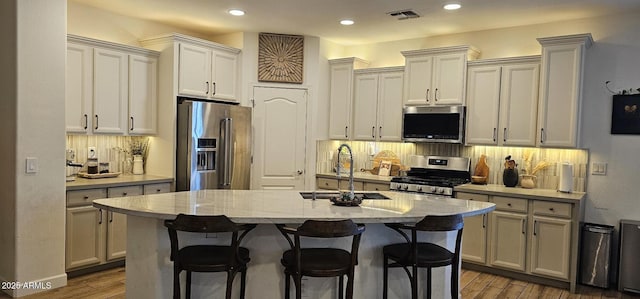 kitchen featuring light stone counters, appliances with stainless steel finishes, dark wood-type flooring, and a kitchen island with sink