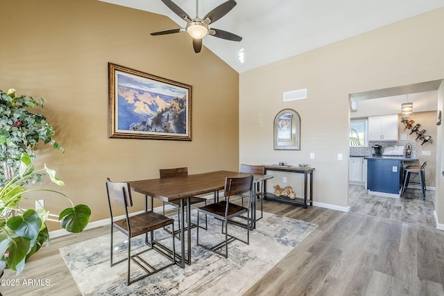 dining area with high vaulted ceiling, ceiling fan, and light wood-type flooring