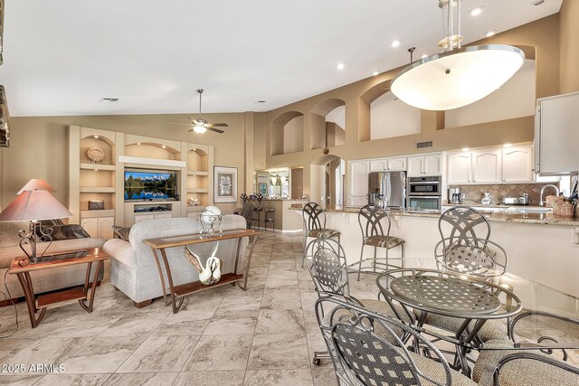 living area with arched walkways, built in features, a ceiling fan, marble finish floor, and vaulted ceiling