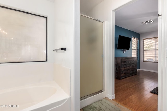 full bath with a garden tub, wood finished floors, visible vents, baseboards, and a stall shower