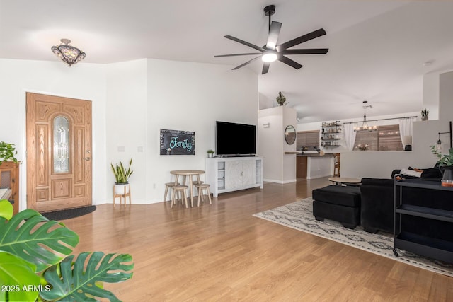 living area with high vaulted ceiling, wood finished floors, and ceiling fan with notable chandelier