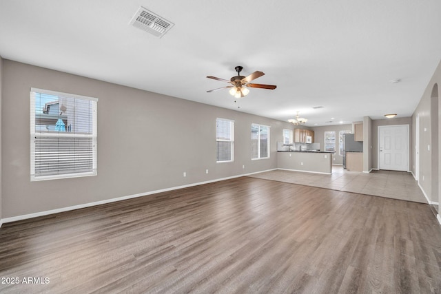 unfurnished living room with ceiling fan with notable chandelier and light hardwood / wood-style flooring