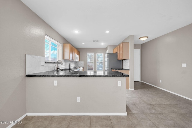 kitchen featuring stainless steel refrigerator, tasteful backsplash, sink, dark stone countertops, and kitchen peninsula