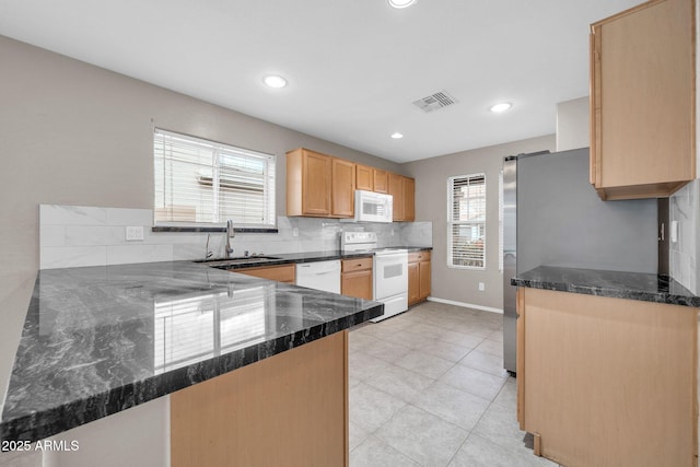 kitchen featuring sink, kitchen peninsula, white appliances, dark stone counters, and decorative backsplash