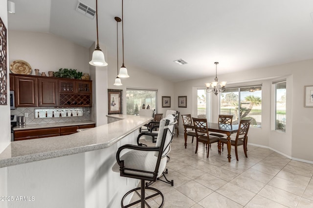 kitchen featuring visible vents, a breakfast bar, backsplash, light tile patterned floors, and lofted ceiling