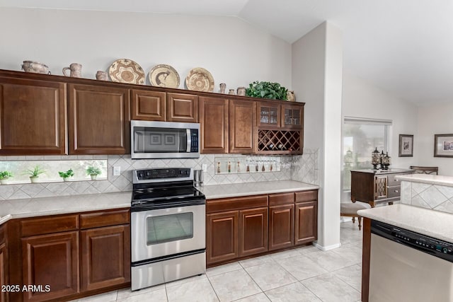 kitchen featuring appliances with stainless steel finishes, light tile patterned flooring, light countertops, decorative backsplash, and lofted ceiling