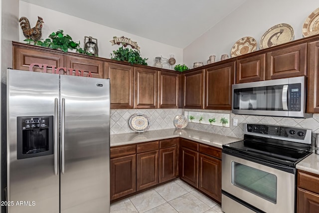 kitchen with backsplash, appliances with stainless steel finishes, light tile patterned flooring, light countertops, and vaulted ceiling