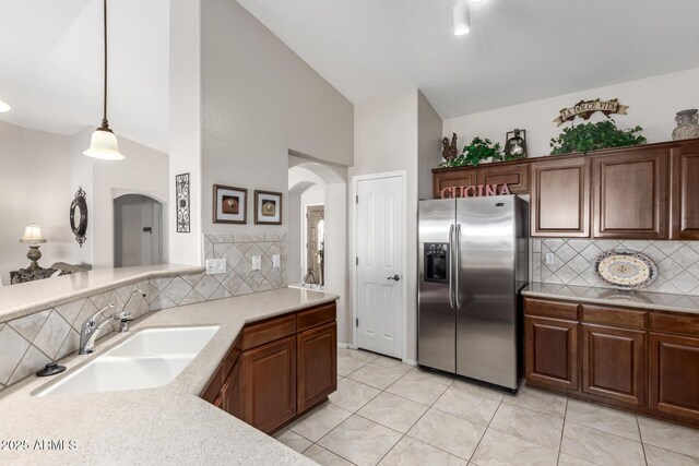 kitchen with tasteful backsplash, pendant lighting, light countertops, stainless steel fridge, and a sink