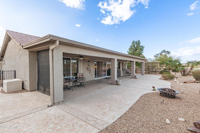 rear view of property featuring a fire pit, a patio, fence, and stucco siding