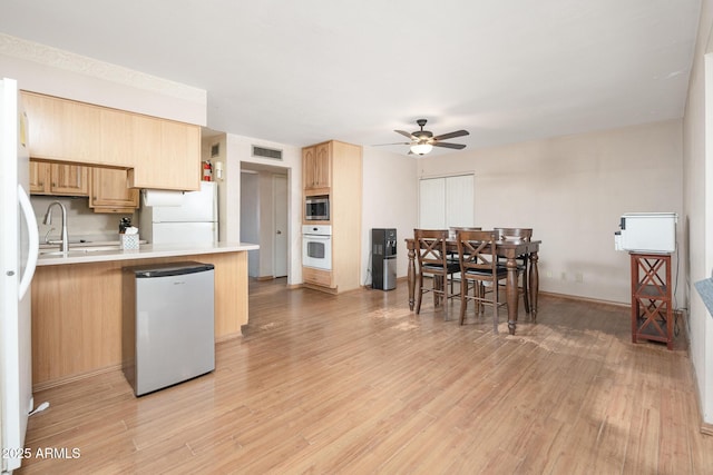 kitchen featuring light brown cabinetry, visible vents, white appliances, and light wood-style floors