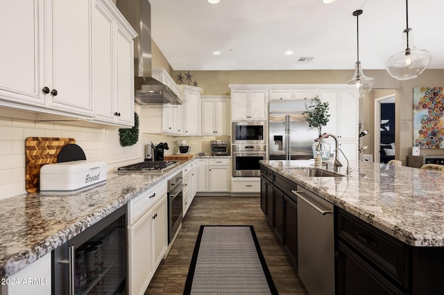 kitchen with backsplash, wall chimney range hood, sink, built in appliances, and a kitchen island with sink