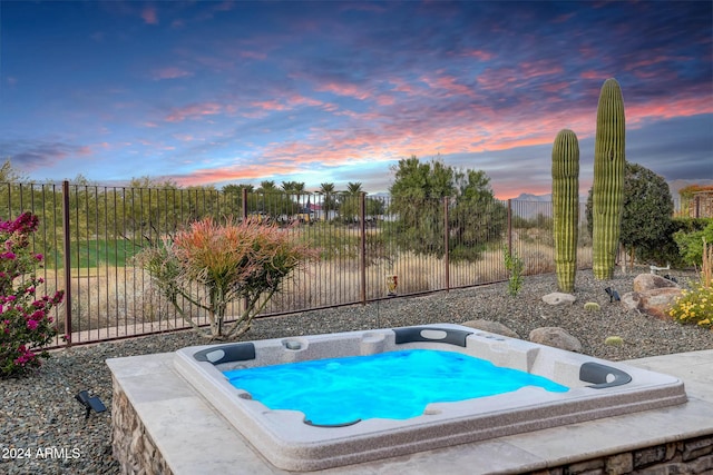 pool at dusk with an outdoor hot tub