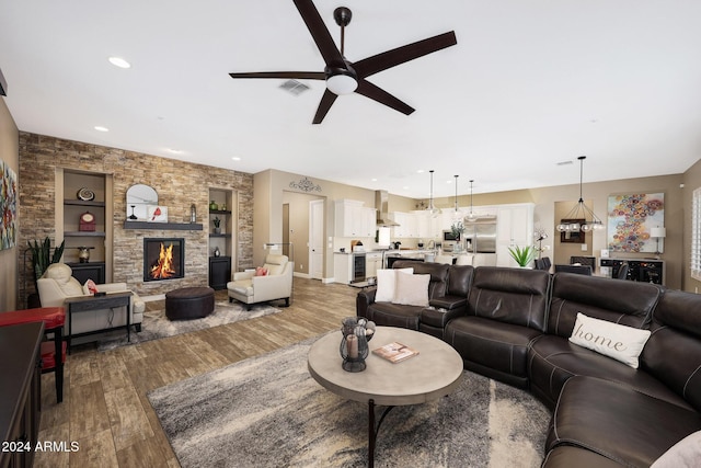 living room featuring built in shelves, wood-type flooring, a fireplace, and ceiling fan with notable chandelier