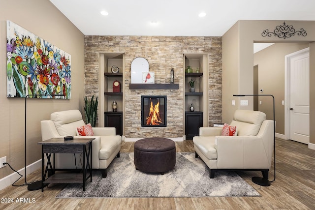 living room featuring wood-type flooring, built in features, and a stone fireplace