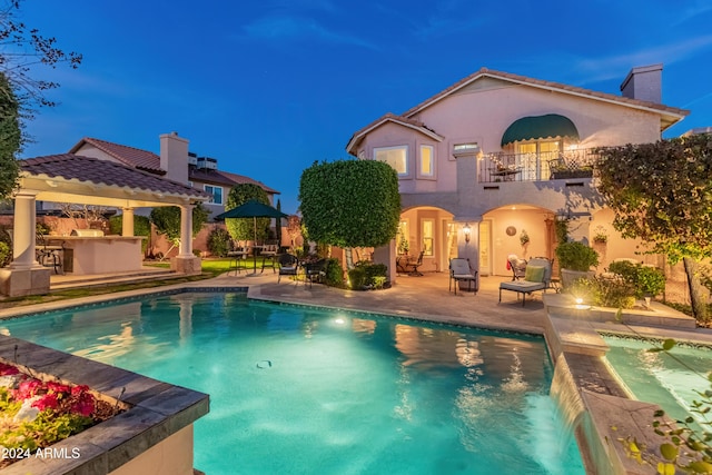 pool at dusk with an outdoor kitchen and a patio area